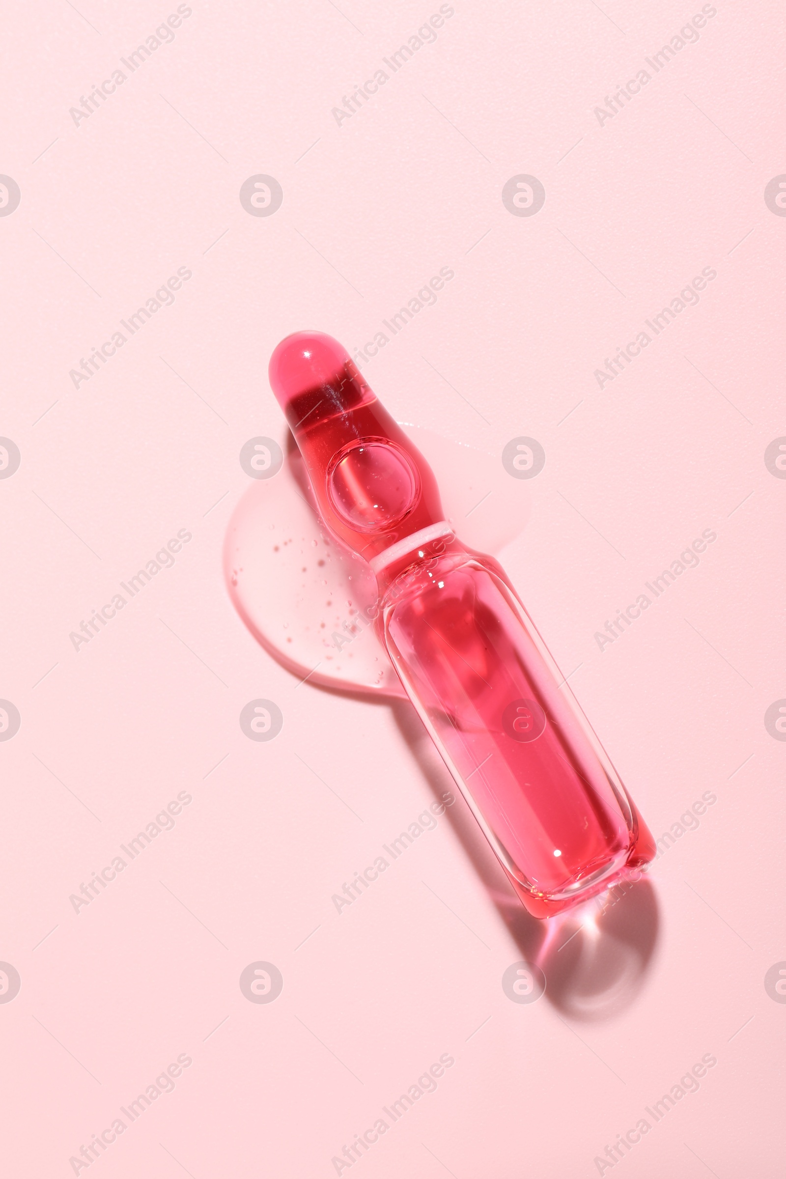 Glass ampoule with liquid on pink background, top view Photo of Glass ampoule with liquid on pink background, top view