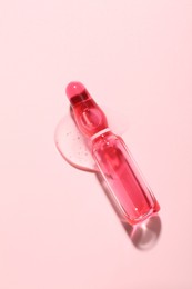 Photo of Glass ampoule with liquid on pink background, top view