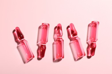 Photo of Glass ampoules with liquid on pink background, flat lay
