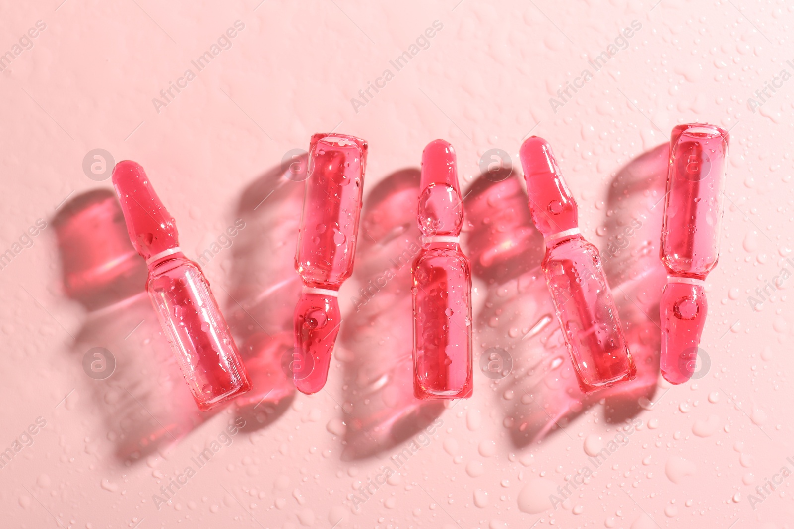 Glass ampoules with liquid and water drops on pink background, flat lay Photo of Glass ampoules with liquid and water drops on pink background, flat lay