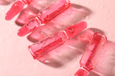 Photo of Glass ampoules with liquid and water drops on pink background, closeup