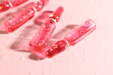 Photo of Glass ampoules with liquid and water drops on pink background, closeup