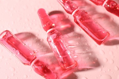 Photo of Glass ampoules with liquid and water drops on pink background, above view