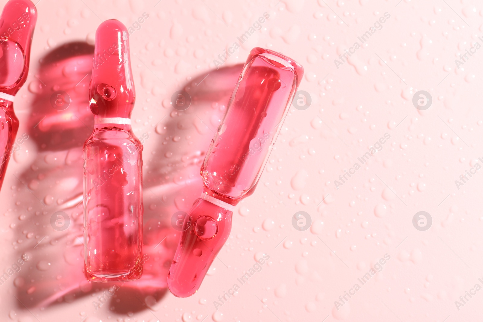 Glass ampoules with liquid and water drops on pink background, flat lay. Space for text Photo of Glass ampoules with liquid and water drops on pink background, flat lay. Space for text