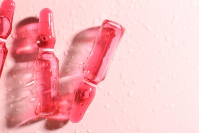 Photo of Glass ampoules with liquid and water drops on pink background, flat lay. Space for text