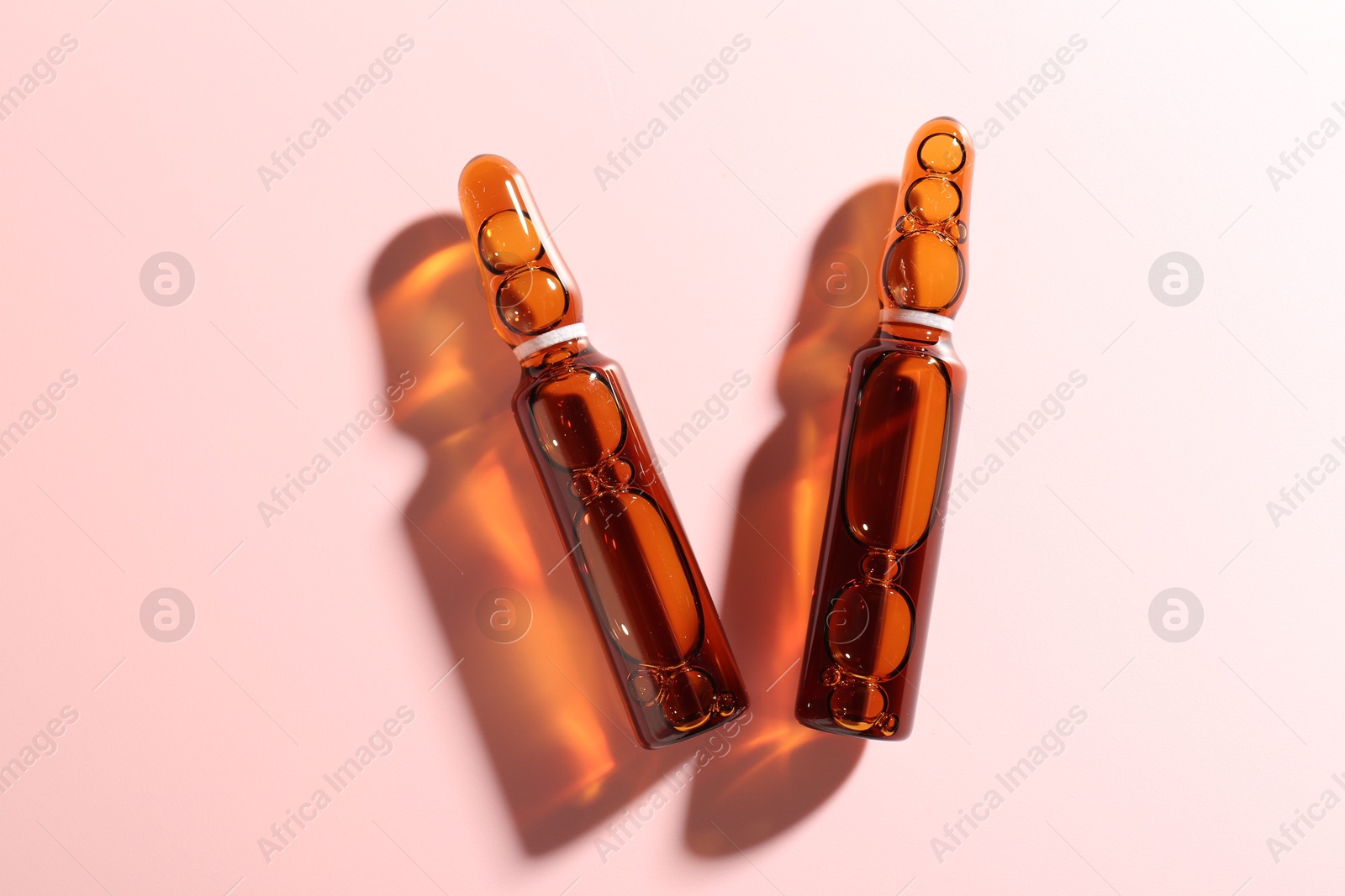 Glass ampoules with liquid on pink background, flat lay Photo of Glass ampoules with liquid on pink background, flat lay