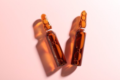 Photo of Glass ampoules with liquid on pink background, flat lay