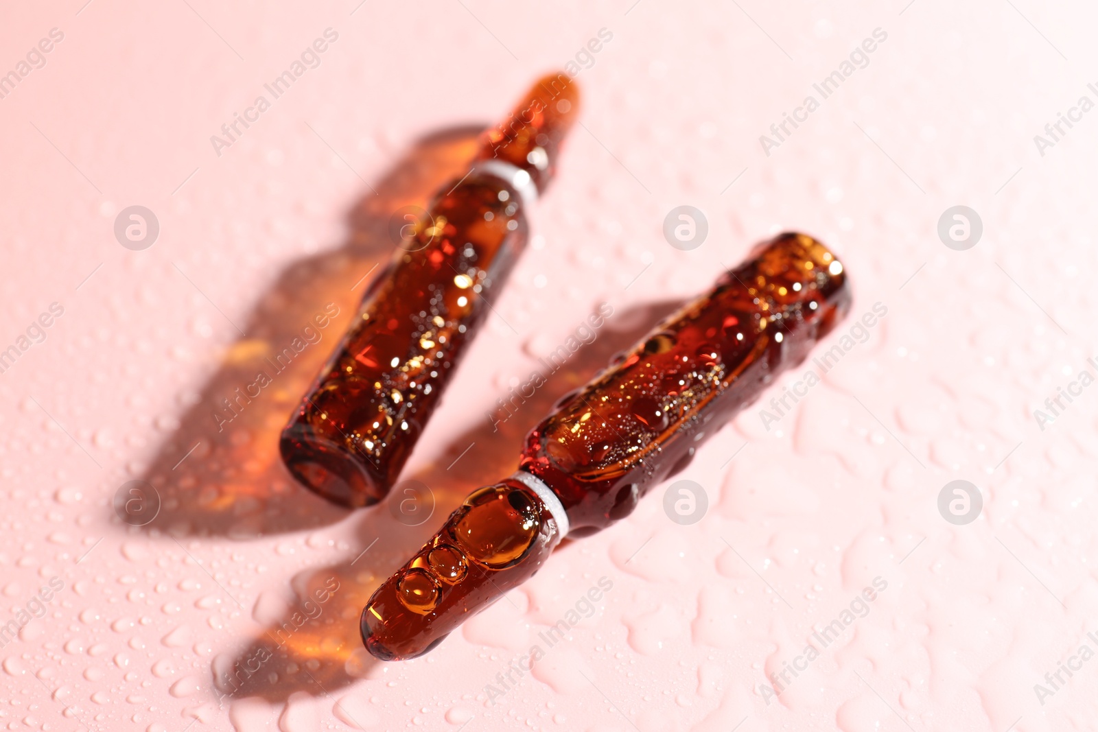 Glass ampoules with liquid and water drops on pink background, closeup Photo of Glass ampoules with liquid and water drops on pink background, closeup