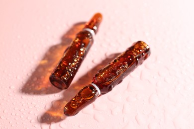 Photo of Glass ampoules with liquid and water drops on pink background, closeup