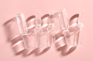 Photo of Glass ampoules with liquid on pink background, flat lay