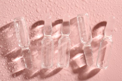 Photo of Glass ampoules with liquid and water drops on pink background, flat lay