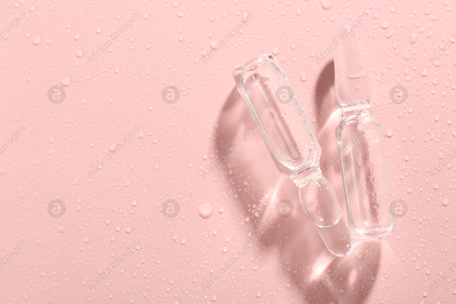 Glass ampoules with liquid and water drops on pink background, flat lay. Space for text Photo of Glass ampoules with liquid and water drops on pink background, flat lay. Space for text