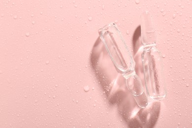 Photo of Glass ampoules with liquid and water drops on pink background, flat lay. Space for text