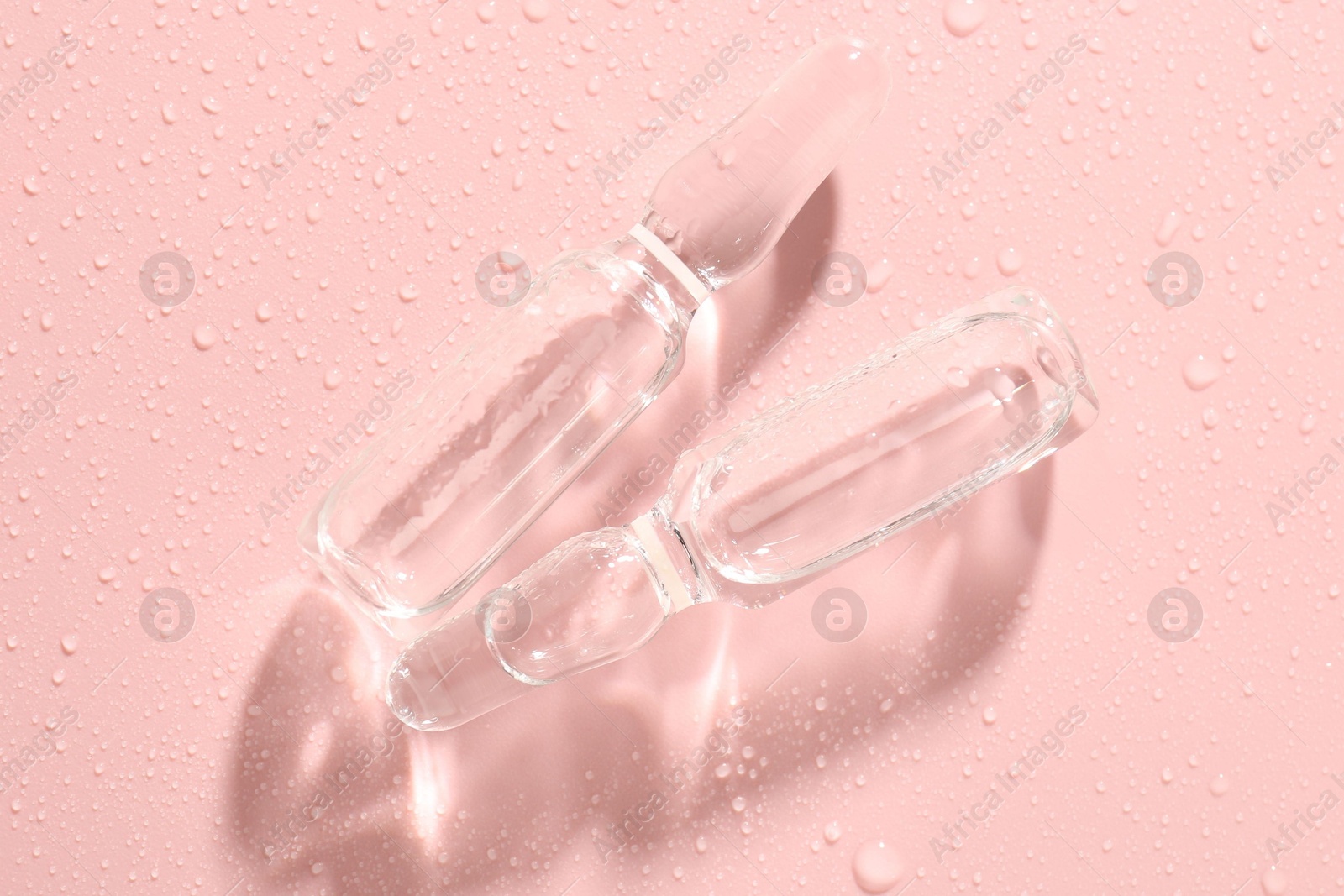 Glass ampoules with liquid and water drops on pink background, flat lay Photo of Glass ampoules with liquid and water drops on pink background, flat lay