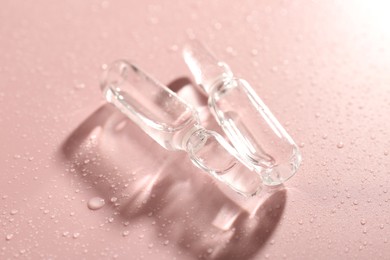 Photo of Glass ampoules with liquid and water drops on pink background, closeup