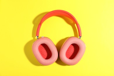 Photo of Pair of stylish pink headphones on yellow background, top view