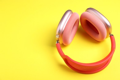 Photo of Pair of stylish pink headphones on yellow background. Space for text