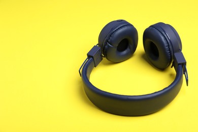Photo of Pair of stylish blue headphones on yellow background. Space for text