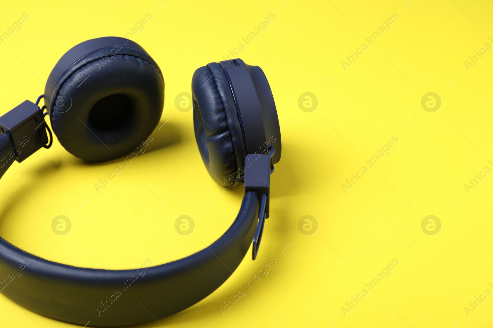 Pair of stylish blue headphones on yellow background, closeup. Space for text Photo of Pair of stylish blue headphones on yellow background, closeup. Space for text