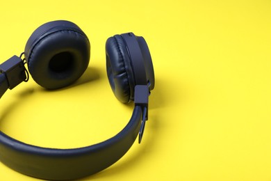 Photo of Pair of stylish blue headphones on yellow background, closeup. Space for text