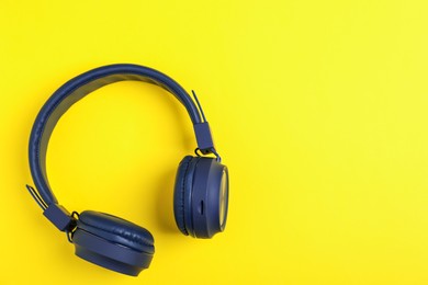 Photo of Pair of stylish blue headphones on yellow background, top view