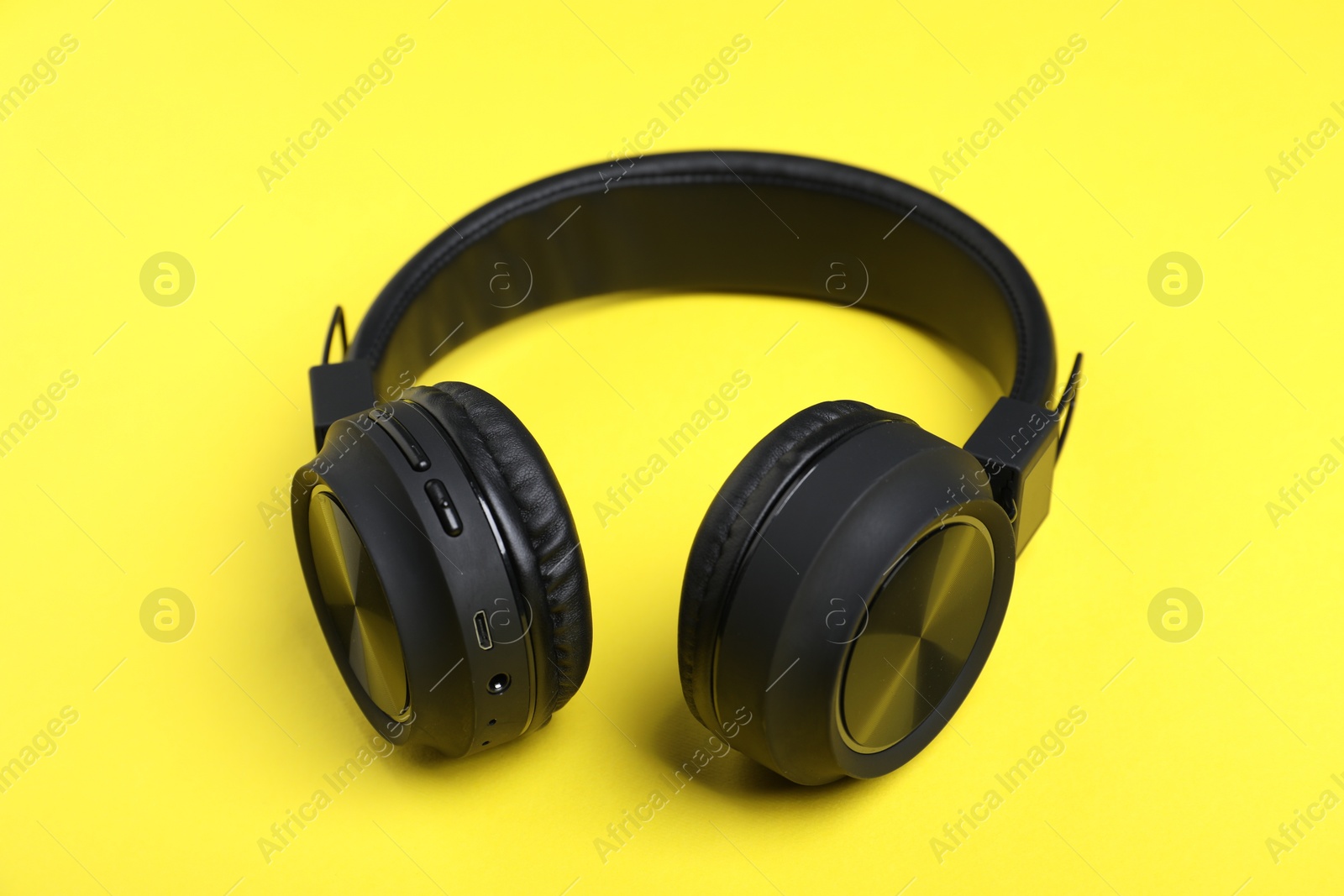 Pair of stylish black headphones on yellow background Photo of Pair of stylish black headphones on yellow background