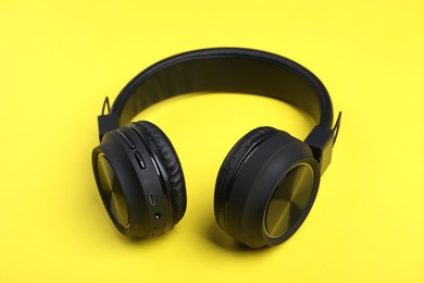 Photo of Pair of stylish black headphones on yellow background