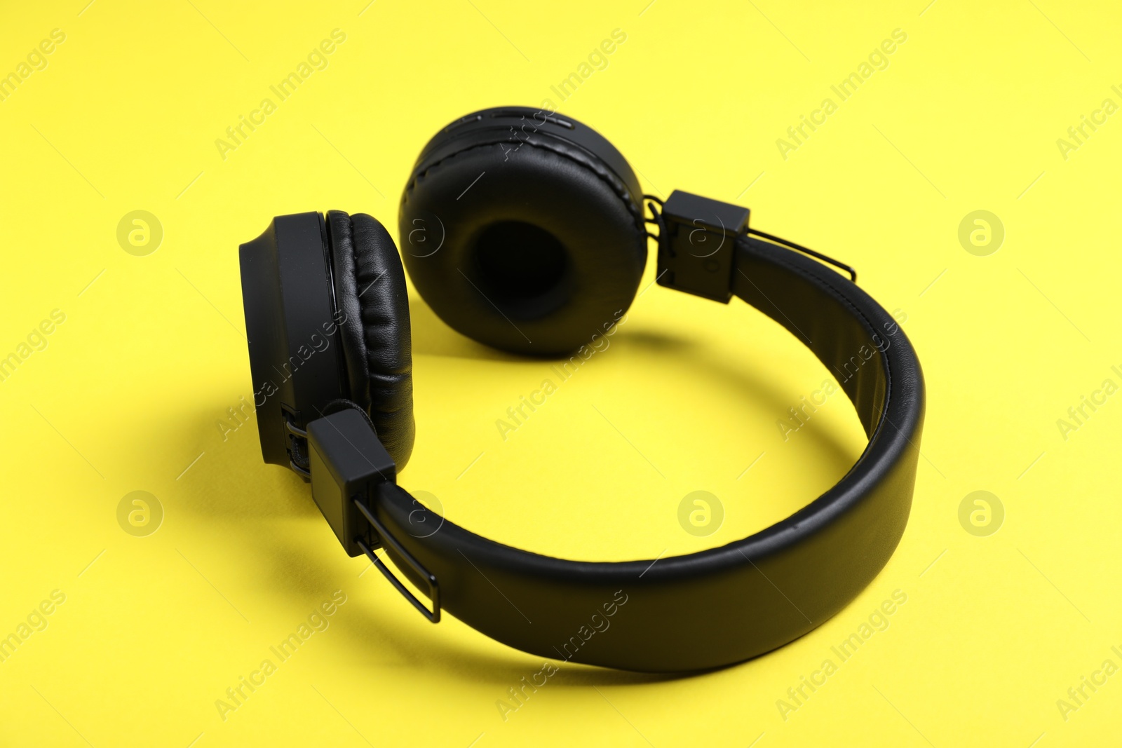 Pair of stylish black headphones on yellow background Photo of Pair of stylish black headphones on yellow background