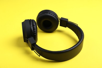Photo of Pair of stylish black headphones on yellow background