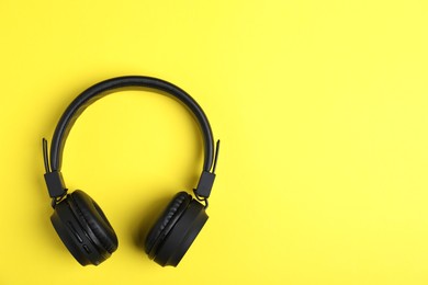 Photo of Pair of stylish black headphones on yellow background, top view. Space for text