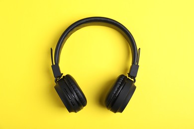 Photo of Pair of stylish black headphones on yellow background, top view