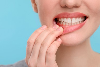 Image of Woman showing inflamed gum on light blue background, closeup