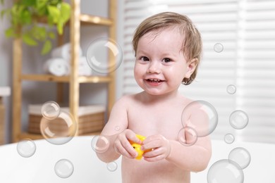 Image of Cute little baby playing with toy duck while taking bath at home. Soap bubbles in air