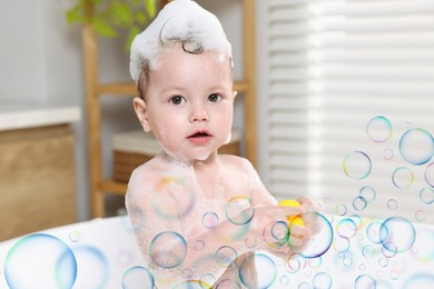 Image of Cute little baby playing with toy duck while taking bath at home. Soap bubbles in air