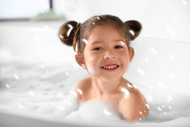 Image of Cute little girl taking foam bath at home. Soap bubbles in air