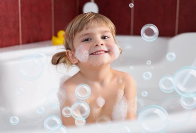 Image of Cute little girl taking bath at home. Soap bubbles in air