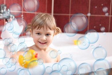Image of Cute little girl taking bath at home. Soap bubbles in air