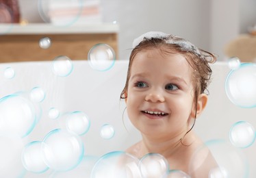 Image of Cute little baby taking bath at home. Soap bubbles in air