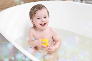 Image of Cute little baby playing with toy while taking bath at home. Soap bubbles in air
