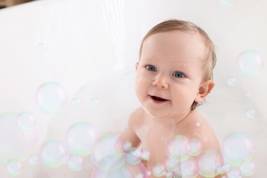 Image of Cute little baby taking bath at home. Soap bubbles in air