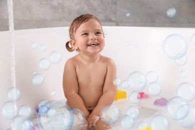 Image of Cute little baby taking bath at home. Soap bubbles in air