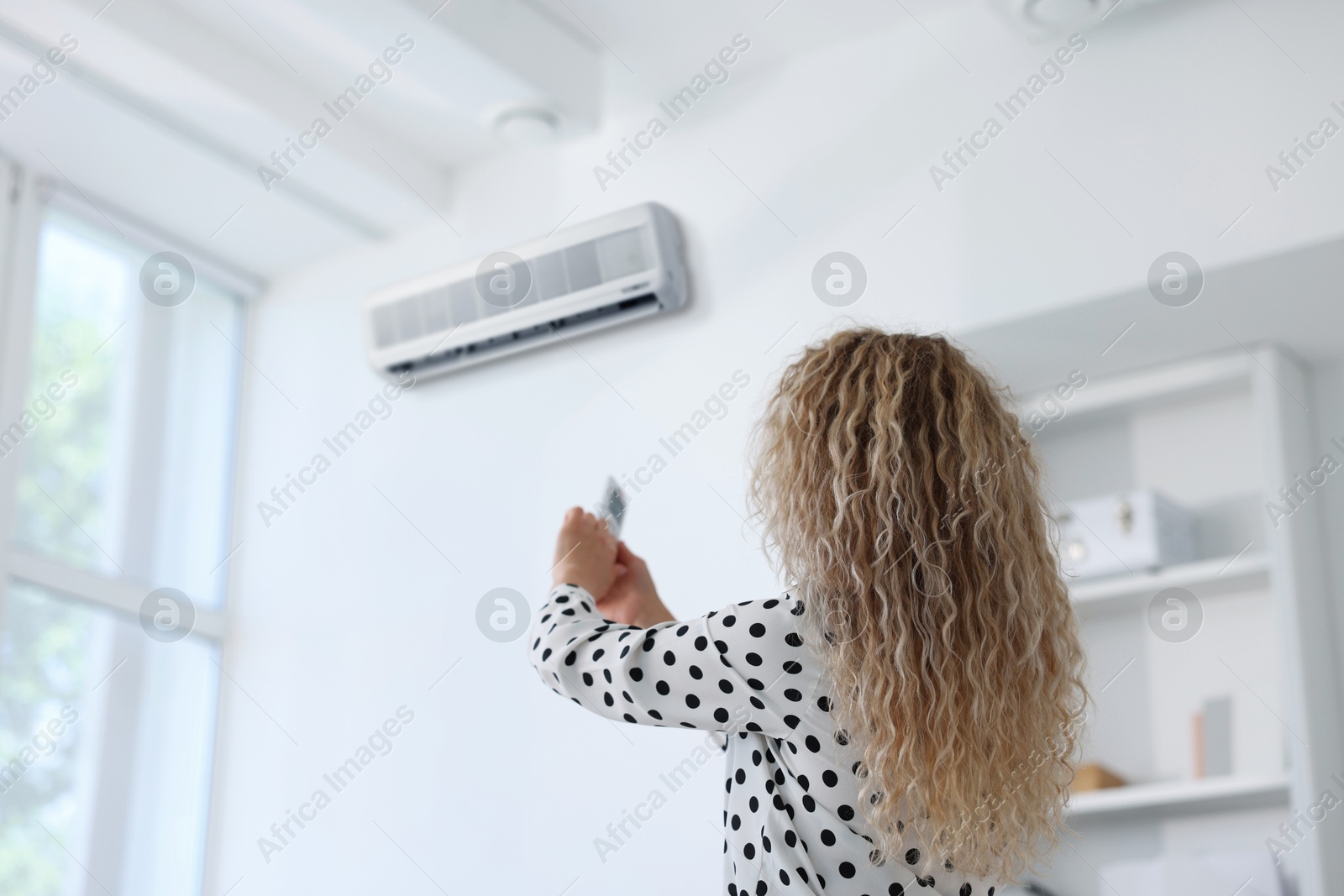 Woman using remote to control air conditioner in office, back view Image of Woman using remote to control air conditioner in office, back view