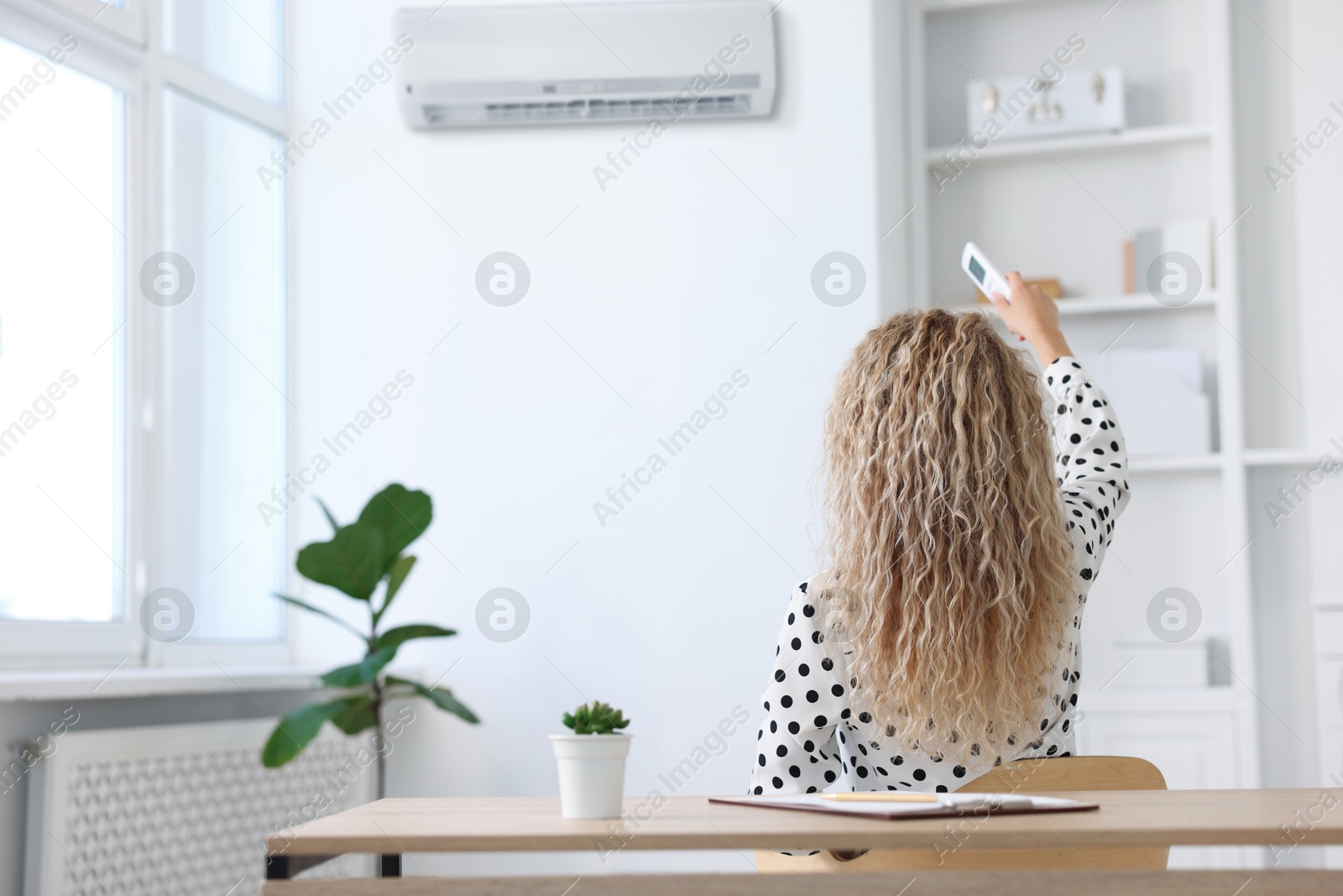 Image of Woman using remote to control air conditioner in office, back view