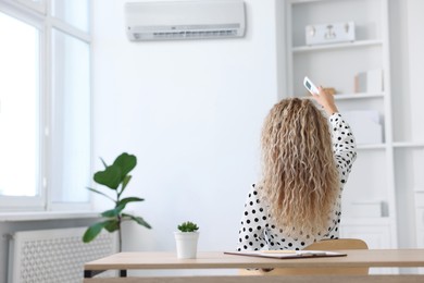 Image of Woman using remote to control air conditioner in office, back view