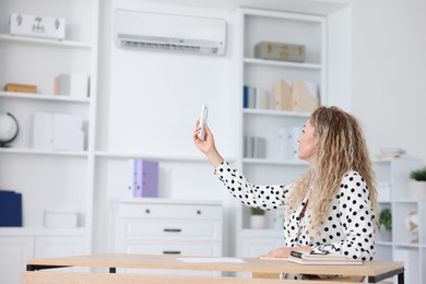 Image of Woman using remote to control air conditioner in office