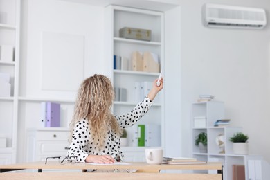 Image of Woman using remote to control air conditioner in office