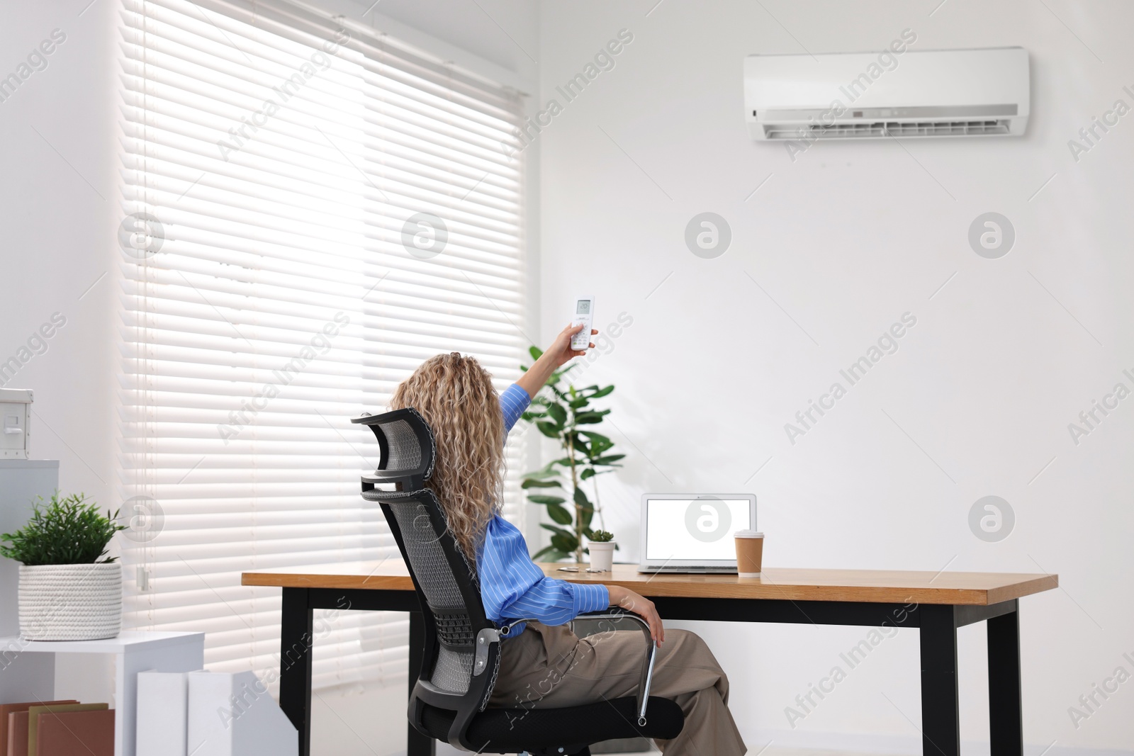 Woman using remote to control air conditioner in office Image of Woman using remote to control air conditioner in office
