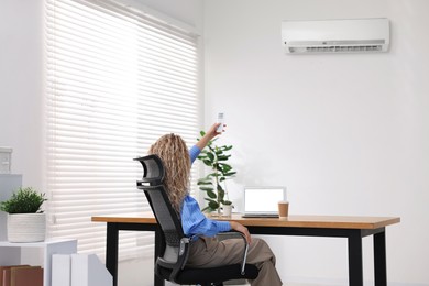Image of Woman using remote to control air conditioner in office