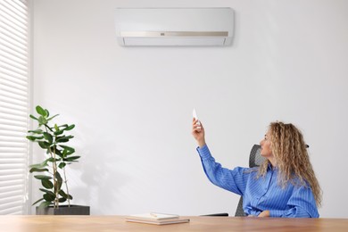 Image of Woman using remote to control air conditioner in office