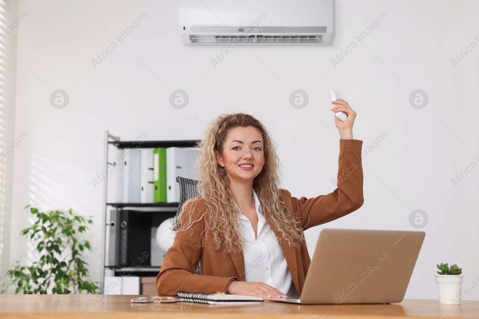 Woman using remote to control air conditioner in office Image of Woman using remote to control air conditioner in office